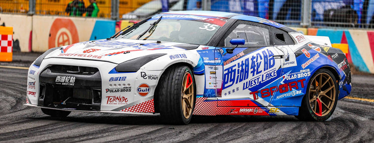 A TTSPORT-branded Nissan GTR race car drifting at high speed, with smoke billowing from the tires, showcasing the control of its high-performance brake system.